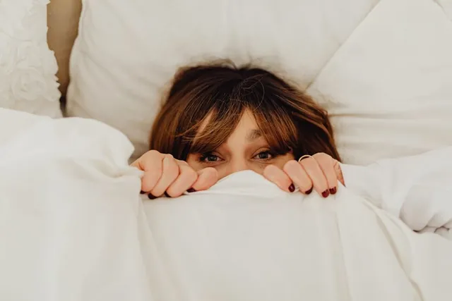 A woman peeking out from under the blanket