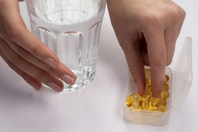 A hand picking a supplement capsule beside a glass of water
